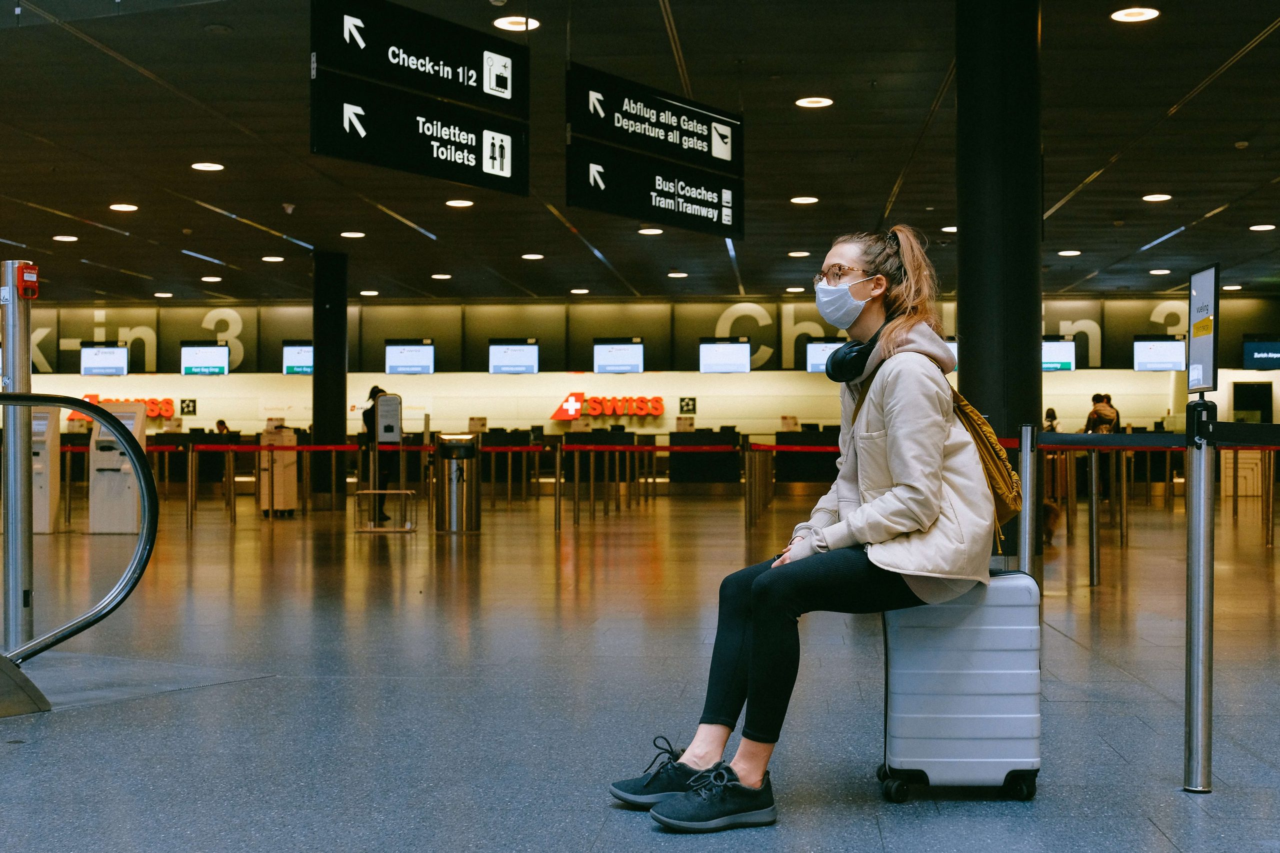 A girl sitting on her luggage, with a mask on her face