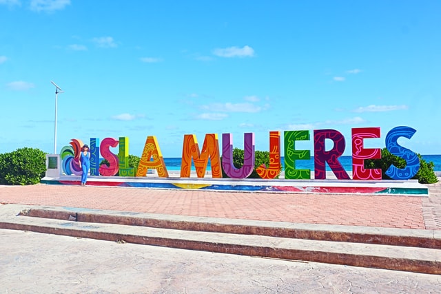 A woman standing next to a colorful sign after visiting Isla Mujeres.