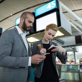 Travelers using a smartphone and holding boarding passes inside an airport terminal