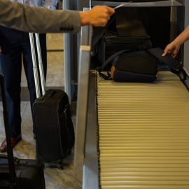 Airport staff assisting passengers with checked luggage on a conveyor belt