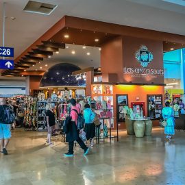 Travelers passing shops and departure-gate signs inside Cancun Airport